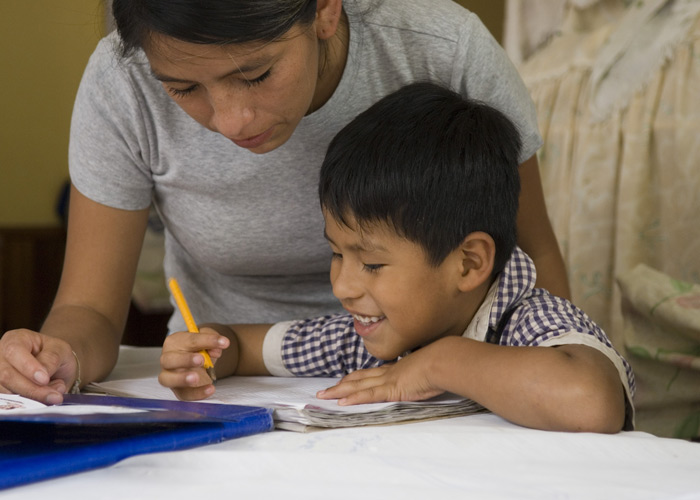 Gutt fra en barneby i Colombia skriver i ei bok. SOS-moren lener seg over ham og hjelper til. Foto: Robert Fleischanderl