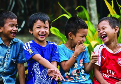 Fire gutter fra SOS-barnebyer Kambodsja i fargerike t-skjorter, står ved sidene av hverandre og ler. 