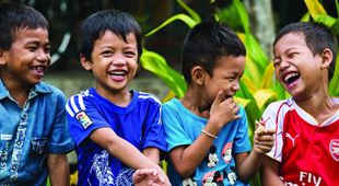 Fire gutter fra SOS-barnebyer Kambodsja i fargerike t-skjorter, står ved sidene av hverandre og ler.
