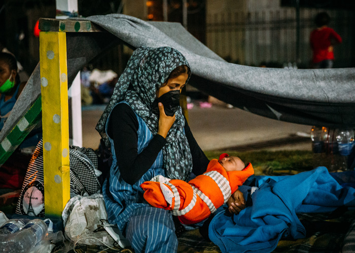 Mor med et nyfødt barn sitter inne i et telt i en flyktningleir på Lesvos. Moren har munnbind og den lille babyen er tullet inn i et organsje teppe. Foto: Alea Horst