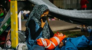 Mor med et nyfødt barn sitter inne i et telt i en flyktningleir på Lesvos. Moren har munnbind og den lille babyen er tullet inn i et organsje teppe. Foto: Alea Horst