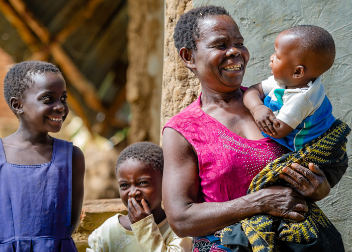 Mor med tre barn, hun har den lille babyen i armene og de to eldste barna smiler. Fra familieprogrammet i Blantyre, Malawi. Foto: Cornel van Heerden