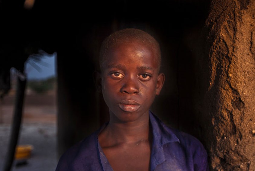 Gutt fra Malawi med et alvorlig uttrykk i ansiktet står lent inntil en vegg laget av leire. Foto: George Kurian 