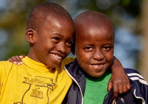 To gutter holder armene over skuldrene til hverandre. Den ene har gul t-skjorte, den andre grønn, begge smiler. Foto: SOS-barnebyer