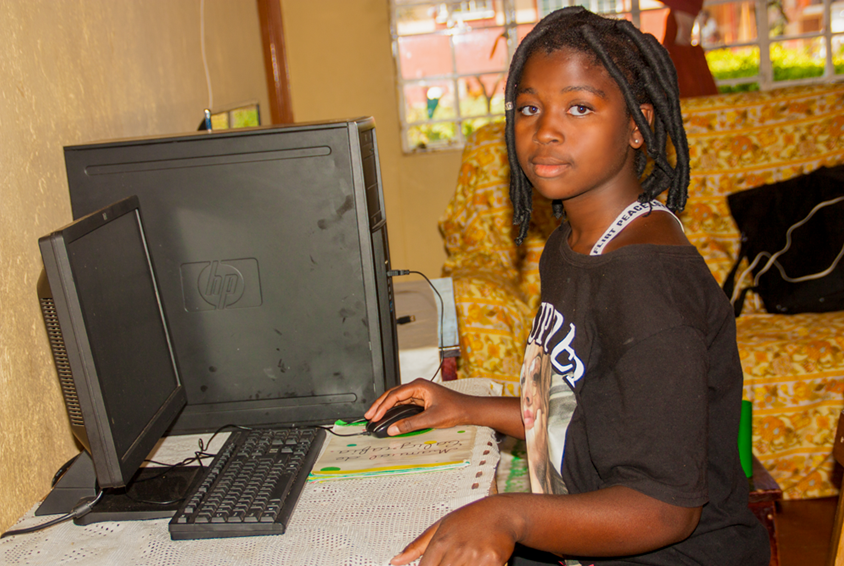 Jente med fletter og sort genser sitter foran en PC. Foto: André Canduco