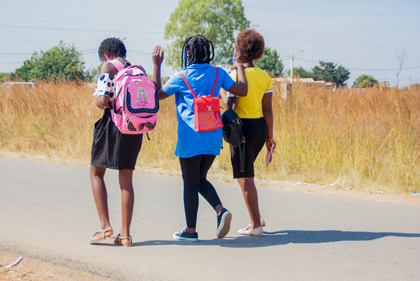 Tre jenter i fargerike klær går langs veien til skolen. Foto: André Canduco