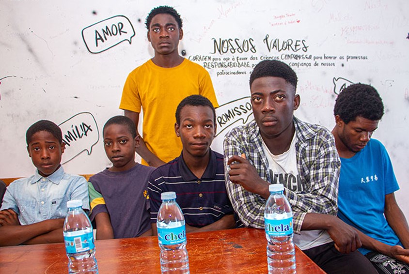 Seks unge gutter sitter ved et bord, i bakgrunnen er det en tavle der det står skrevet temaer de har snakket om. Foto: Pedro Canjeque