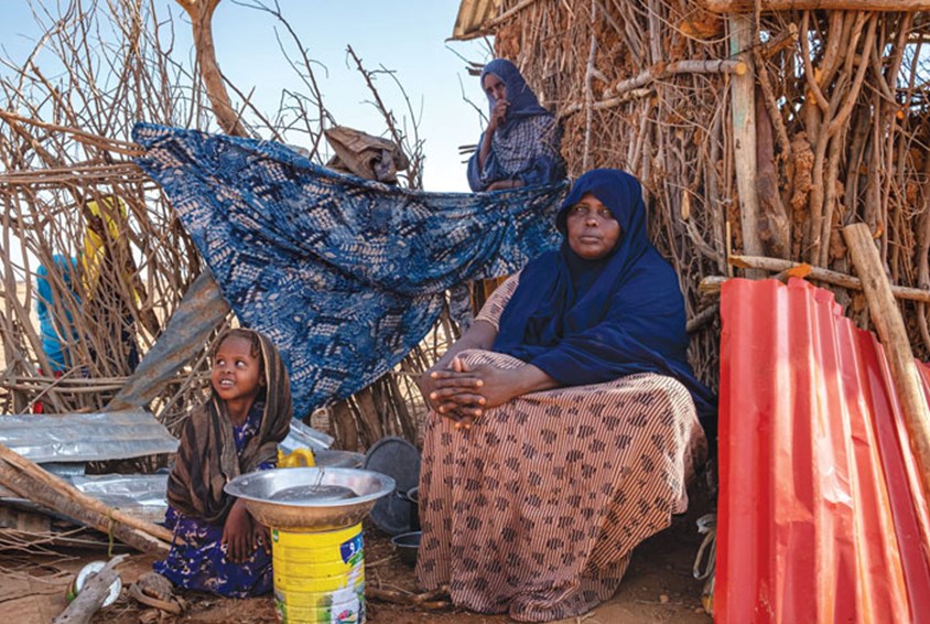 To kvinner fra Etiopia, begge med hijab, sitter foran ei hytte laget av kvister, ei lita jente sitter på bakken . Det er veldig tørt. Foto: Joost Bastmeijer
