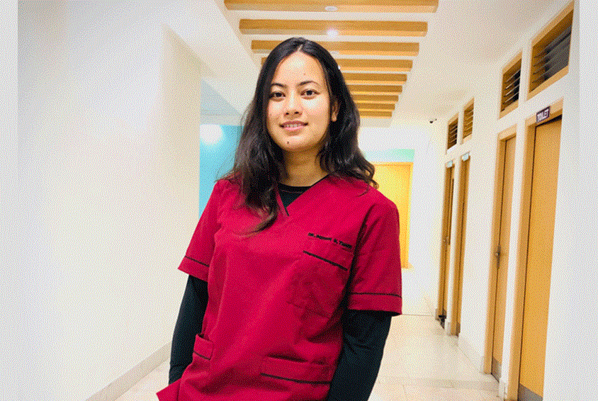 Ung kvinne med mørkt, langt hår står i en sykehuskorridor, hun har på seg dyp rosa uniform. Illustrasjonsfoto: SOS-barnebyer