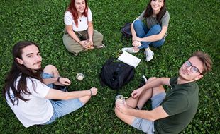 To unge jenter og to unge gutter sitter på gresset i en ring og titter opp på den som tar bildet. Foto: Katerina Ilievska