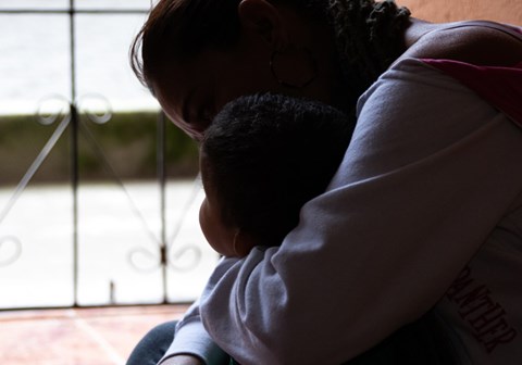 Mor holder barnet sitt tett inntil seg og ser ut av et vindu. Illustrasjonsfoto: SOS-barnebyer