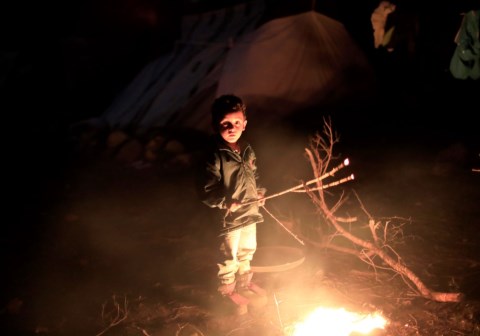 Liten gutt står ved flammene. Støtt barna i Moria. bilde Giorgos Moutafis