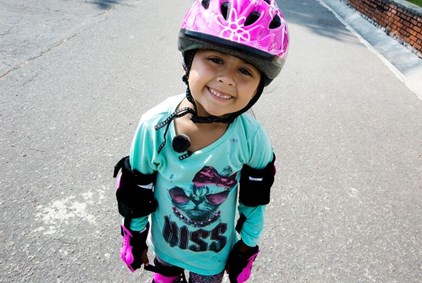 En jente på rulleskøyter med rosa hjelm og turkisgrønn t-skjorte.