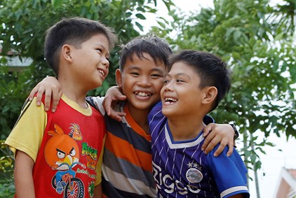 Tre gutter fra Vietnam i fargerike t-skjorter holder rundt hverandre.