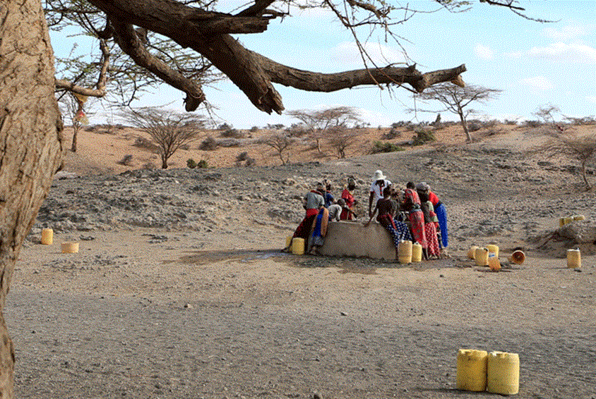 Kvinner står rundt en brønn og heiser opp vann. Landskapet rundt dem er helt uttørret. Foto: Noor Kamis