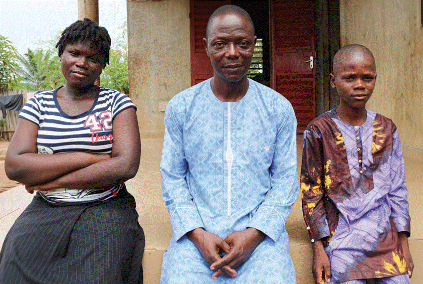 Bernard sitter foran huset sitt sammen med to av barna sine. Foto: SOS-barnebyer