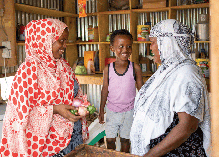 En mor og sønnene hennes ser på hverandre og smiler. De er i den lille butikken moren driver og betjener en kunde som har kjøpt løk og paprika. Foto: Lydia Mantler