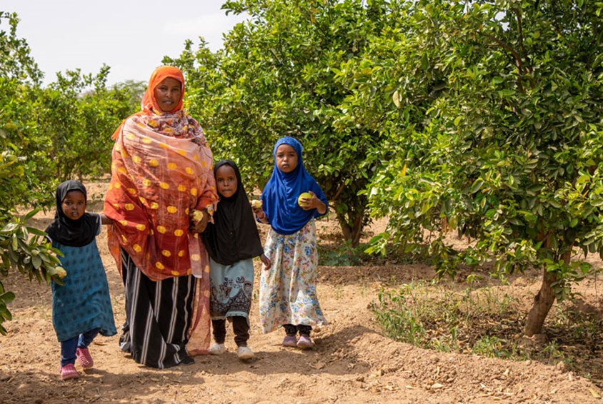 Aamina, to søstre og moren går på stien mellom frukttrærne. Foto: Lydia Mantler