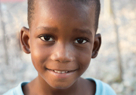 Andre har på seg lyseblå t-skjorte og smiler sjenert til kameraet. Foto: SOS-barnebyer Haiti
