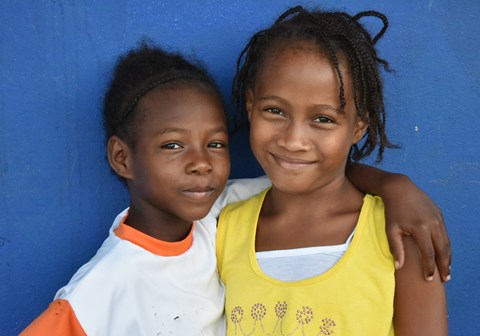 To smilende jenter fra Colombia, i SOS-barnebyer. Smilende foran en blå vegg. Foto: Daniel Castaño Leal. 