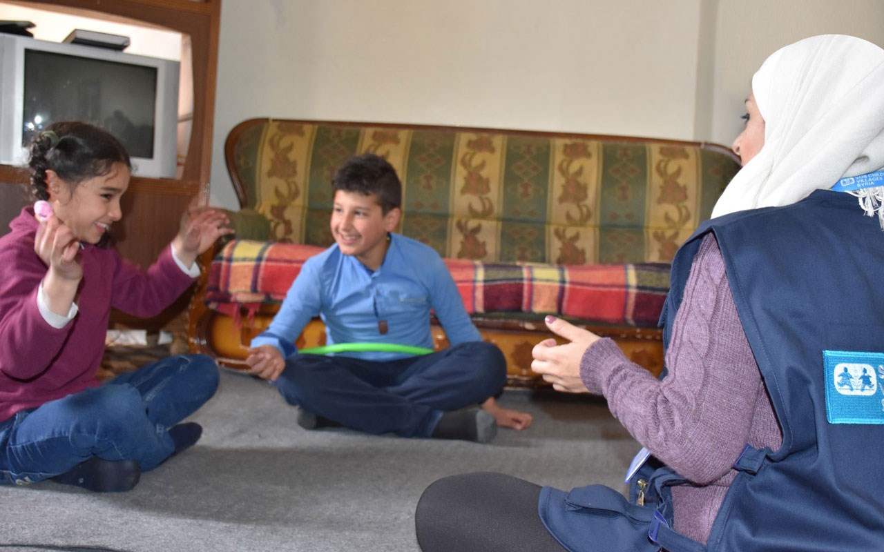 To barn sitter på gulvet sammen med en sosialarbeider fra SOS-barnebyer. Foto: SOS-barnebyer
