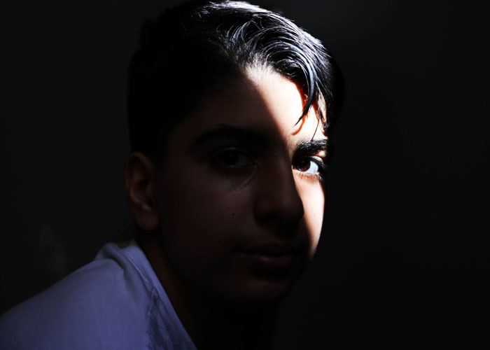 Portrett av gutt som ser alvorlig inn i kamera, halve ansiktet har en mørk skygge. Foto: Giorgos Moutafis