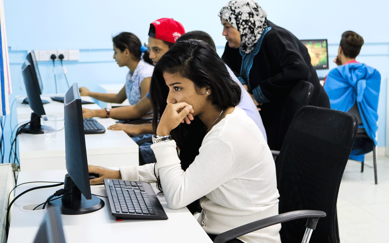 Ei jente fra Jordan, med mørkt langt hår og hvit genser, sitter foran PCen. Foto: Lydia Mantler