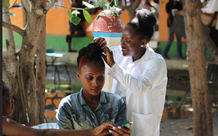 Ei ung jente i hvit frakk setter opp håret til en kunde. Foto: SOS-barnebyer Haiti