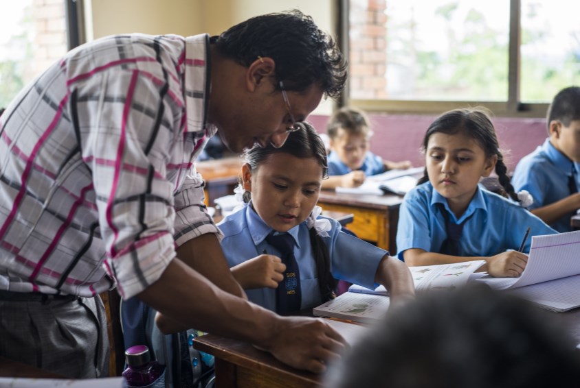 Usha* 10 år, diskuterer skolearbeidet med læreren sin. Hun mistet hele familien sin, da huset de bodde i kollapset under jordskjelvet i Nepal. Nå bor hun i SOS-barnebyen Sanothimi i Bhaktapur og har fått en ny familie, oppfølging og omsorg. Foto: Suzanne Lee (*Navnet er endret)