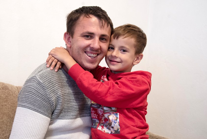 Nurija, smiler stort og gir sønnen sin en klem. Han har på seg hvit og grå genser, sønnen rød genser. Foto: Katerina Ilievska