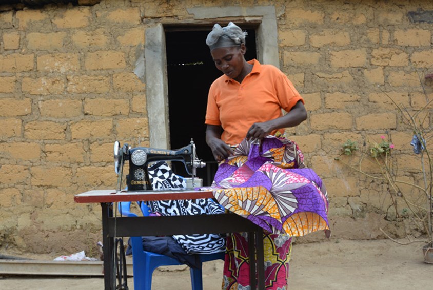 Barnabyeh står utenfor huset sitt og syr på symaskinen hun har fått støtte til å kjøpe seg gjennom SOS-barnebyers familieprogram i Huambo, Angol. Foto: Turid Weisser