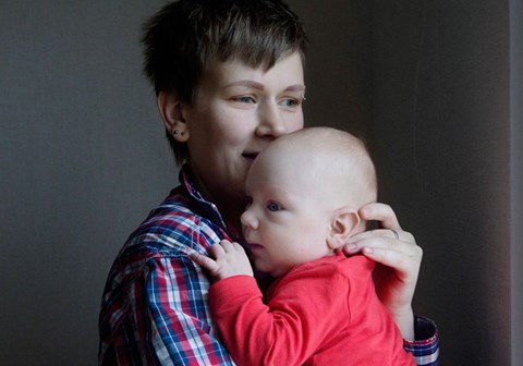Yekaterina holder den lille babyen tett inntil seg. Hun har på kortklippet sveis, og har på seg rutet skjorte, babyen har rød genser og blå joggebukse. Foto: Nina Ruud
