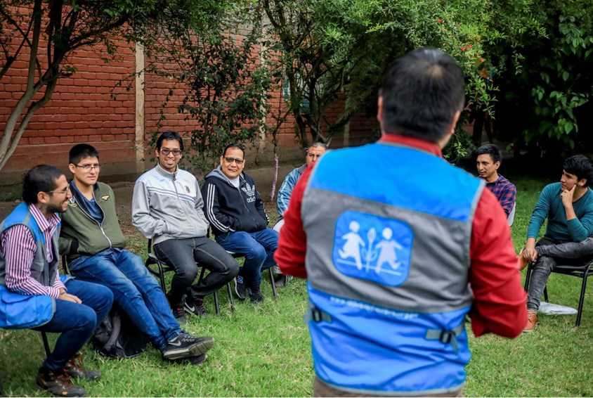 Menn sitter på plaststoler i en sirkel, de deltar på workshop i pappaprogrammet i Peru.