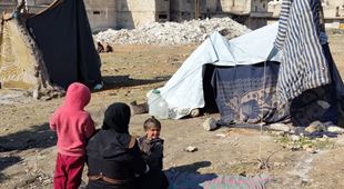 En mor og to barn sitter på bakken i et område hvor det er satt opp provisoriske telt. Foto Mahmoud Shabarek