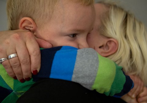 En mor med lyst hår holder rundt sønnen sin og klemmer han inntil seg. Han har kort lyst hår og stripete genser. Foto Katerina Ilievska
