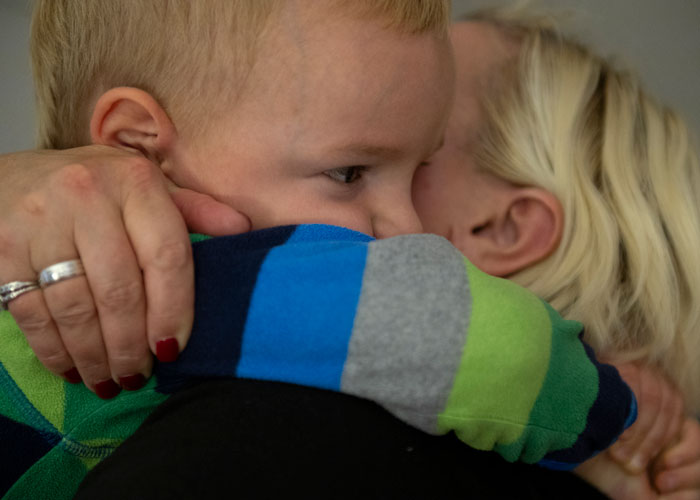 En mor med lyst hår holder rundt sønnen sin og klemmer han inntil seg. Han har kort lyst hår og stripete genser. Foto Katerina Ilievska
