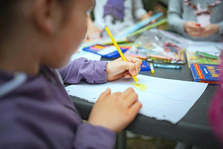 Jente fra Ukraina i lilla genser og fletter sitter ved et bord og tegner. Foto: SOS-barnebyer