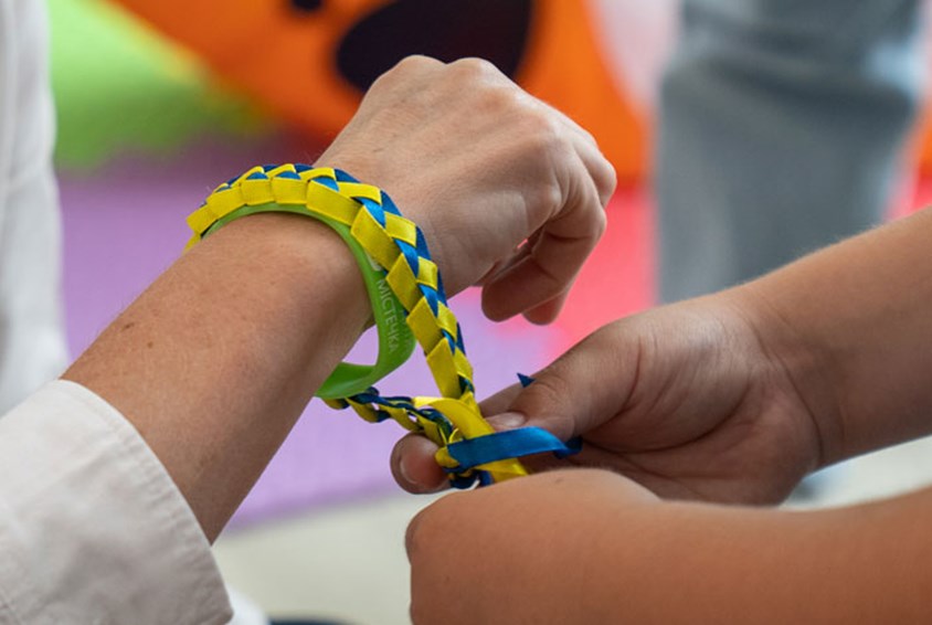 To hender som knytter et flettet bånd i gult og blått rundt håndleddet til en annen. Foto: Oleksandra Zborovska