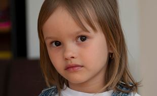 Alvorlig jente med halvlangt hår, hvit t-skjorte og blå selebukse. Foto: Katerina Ilievska