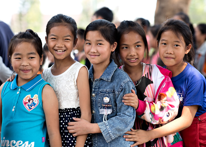 Fem jenter fra Laos står og holder rundt hverandre. de har på seg fargerike klær og smiler. Foto: Lars Just