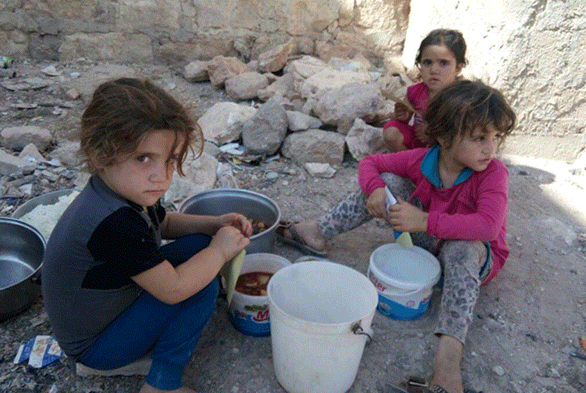 Tre jenter sitter på bakken og spiser mat de har fått utdelt i plastbøtter. Foto: SOS-barnebyer Syria