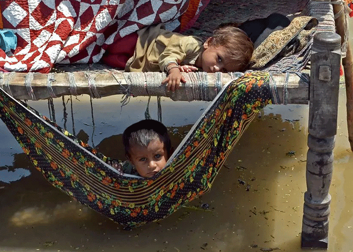 Flom i Pakistan: To barn ligger i en provisorisk beskyttelse som står på påler, det er vann på alle kanter. Foto: Naseebullah Jamali
