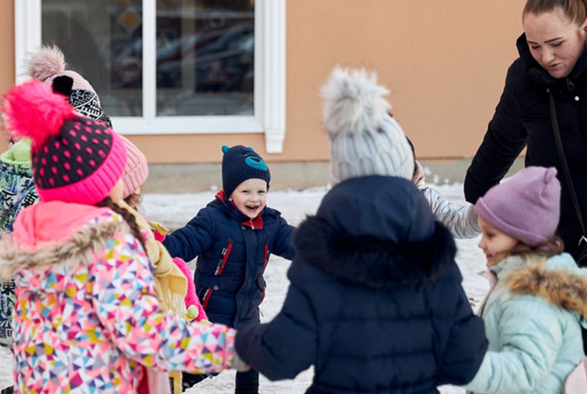 Barn fra Ukraina står i en ring og holder hverandre i hendene, en medarbeider fra SOS-barnebyer står sammen med dem. Det er vinter og alle har på seg viinterklær. Foto Roksolyana Trush