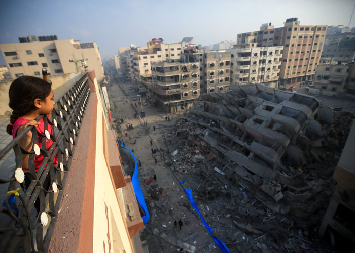 Jente med mørkt hår i en flette og rød t-skjorte,  og står på et tak og ser ut over alle ødeleggelsene. Foto: Mohamed Zaanoun Middle EastImages via AFP