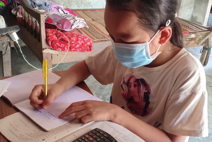 Linh 12 år sitter ved pulten sin hjemme og gjør lekser. Hun har på seg munnbind. Foto: Pearl Sandhu Anne Kahura